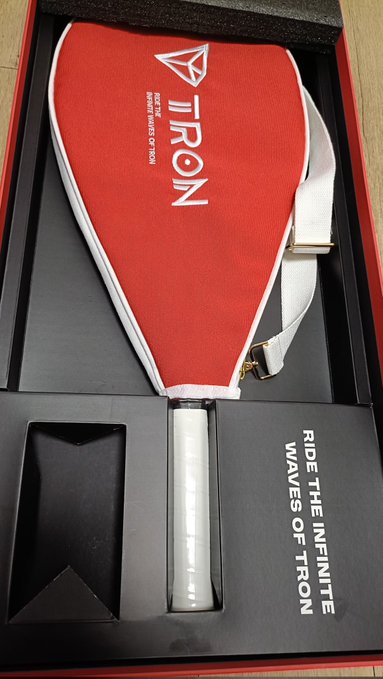 A red "IRON" pickleball paddle (Tron Inc.'s brand) sits in its packaging, which reads "RIDE THE INFINITE WAVES OF TRON" and "TRON INC | RIDE THE WAVES OF TRON," serving as a souvenir from Tron's 3rd offline cruising event.