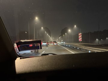 Nighttime view from inside a vehicle driving on a highway, showing road construction with warning barriers and street lights illuminating the route ahead.