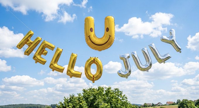 Gold and silver foil balloons spelling 'HELLO U JULY' (with a smiley face balloon for the U) floating against a blue sky with clouds.