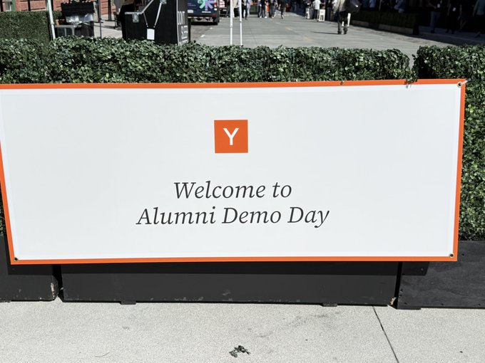 A welcome banner for "Alumni Demo Day" at Y Combinator stands on a sidewalk, with the company's orange "Y" logo prominently displayed. The image fits the post's sentiment perfectly—despite trying to move on from YC as an alumnus, the community keeps drawing founders back for events like Demo Day.