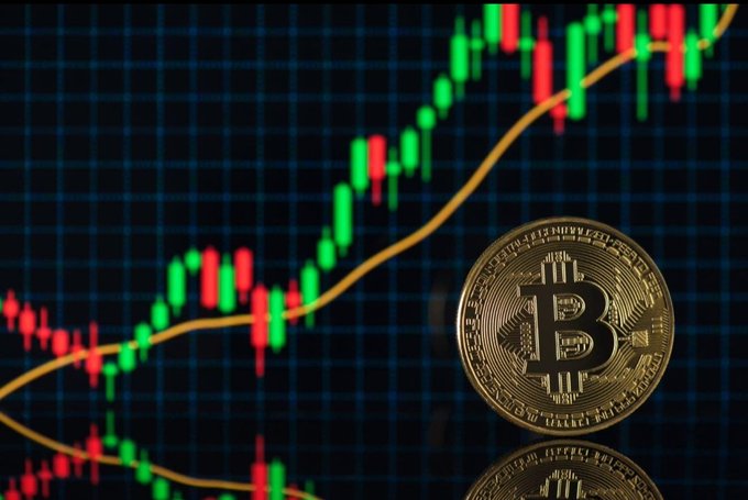 A gold Bitcoin coin sits in front of a candlestick chart showing an upward price trend, visually reinforcing the post's message about Bitcoin's recovery above $64,000 and its resilience against Strategy's recent BTC sale.