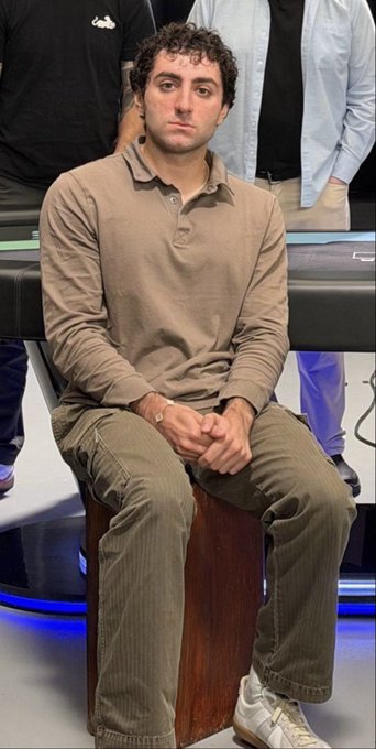 A man in a beige polo shirt and olive pants sits stiffly on a wooden stool with a nervous, deer-in-headlights expression and clasped hands, looking utterly unenthused despite being surrounded by people. His tense, uncomfortable posture humorously contrasts with the post's joke about acting eager for attention only to freeze up when it actually arrives.