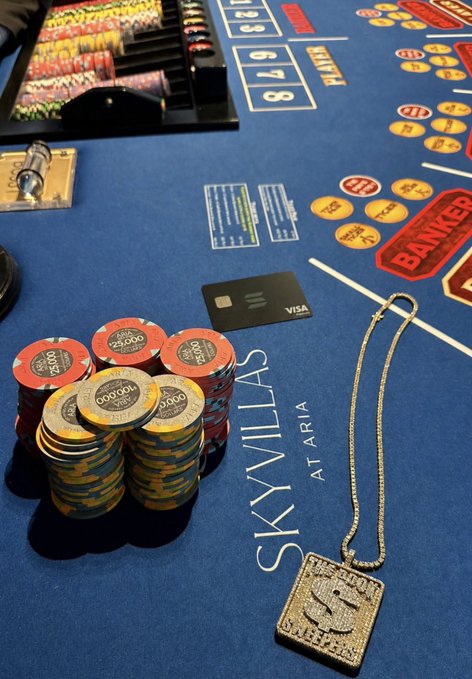 A poker table with a blue felt surface, featuring a stack of red and yellow chips, a black credit card, and a silver chain necklace.