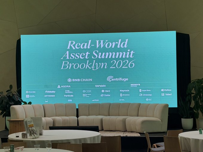 An event space features a large screen displaying 'Real-World Asset Summit Brooklyn 2026' along with sponsor logos like BNB CHAIN and Centrifuge.