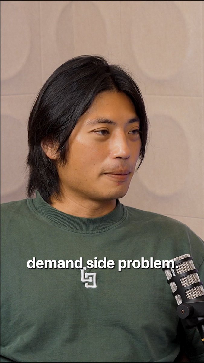 A man with long dark hair wearing a green sweatshirt sits in front of a microphone, looking off to the side. The caption "demand side problem" appears across his chest, illustrating the podcast conversation about the chicken-and-egg platform challenge of supply versus demand.