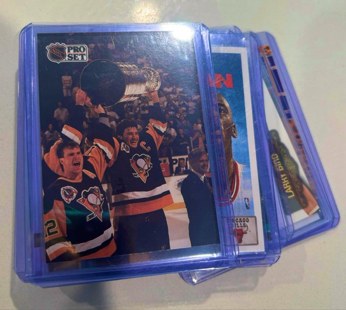 Hockey trading cards in protective sleeves are stacked, with the top card showing Pro Set NHL players lifting the Stanley Cup, including a Pittsburgh Penguins captain.