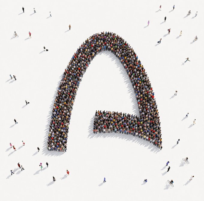 An aerial conceptual image of hundreds of people arranged in the shape of the Aptos (APT) logo, a stylized letter "A" on a white background.