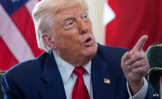 Donald Trump, wearing a dark suit and red tie with a small American flag pin, points his finger while speaking, with an American flag visible in the background and the AFP logo in the bottom right corner.