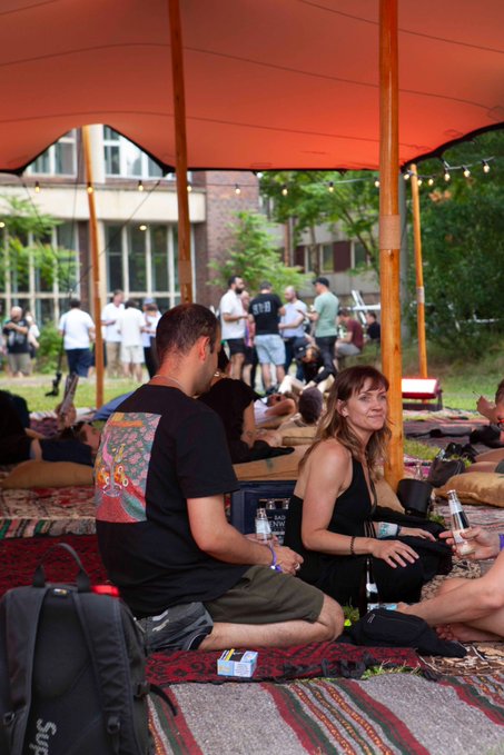A diverse group of attendees relaxes on patterned rugs and cushions under a red canopy at Funkhaus during the Web3 Summit, where Astral Industries created "Space to Think" with soft seating for casual conversation and ambient reflection between the day's big ideas.