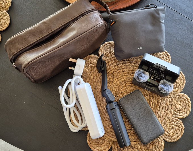 Tech essentials laid out on a woven mat, including a DJI pouch, an audio recorder with furry windscreens, a gimbal, a power bank, cables, and a leather dopp kit—gear being packed for Token2049 to represent Midnight Network ($NIGHT).
