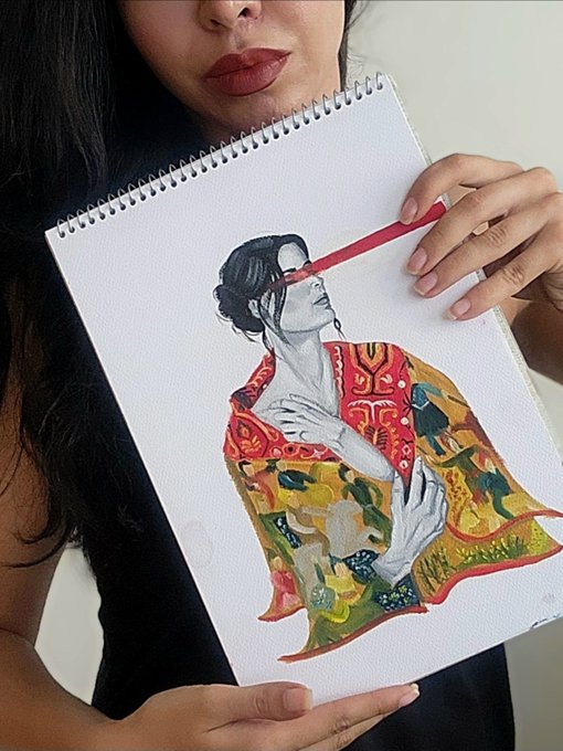 A woman holding a sketchbook displaying an artwork of a figure in a colorful yellow and red patterned robe, with a red colored pencil held up to her lips.