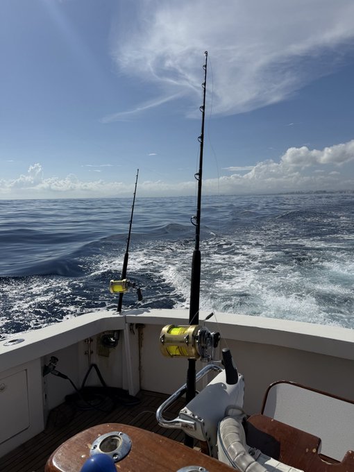 Two fishing rods with yellow reels trail behind a boat cutting through open ocean. The post’s line, “Doing my best to try and touch some fish today,” captures the hopeful offshore fishing attempt.
