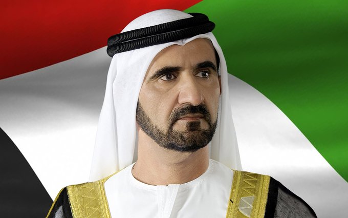 A portrait of a man wearing traditional Emirati attire (white kandura and ghutra with black agal) in front of the UAE flag.