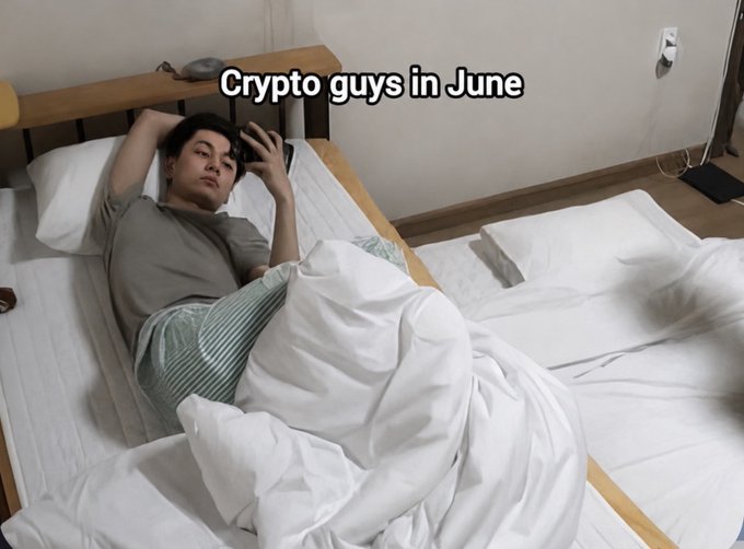 A meme showing a young man lying in bed on his phone with the caption 'Crypto guys in June'.