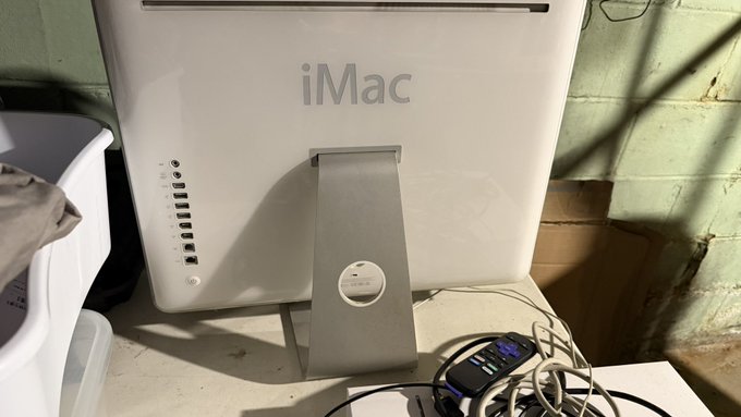 The back of a white iMac computer with its stand visible, sitting on a desk next to a blood glucose meter and tangled wires.