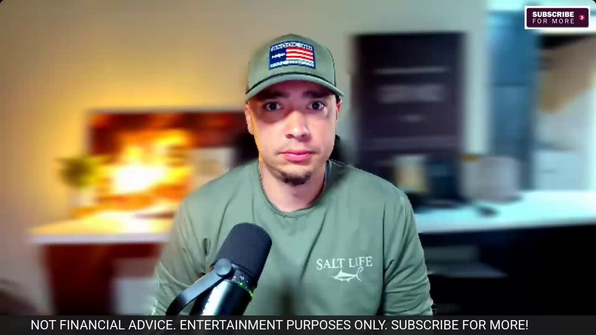 The image shows a man wearing a green shirt standing behind a microphone, likely participating in an online podcast or live stream event. He has a serious expression as he appears to be discussing a new cryptocurrency called RippleXRP. The man also wears a cap with an American flag design on it and speaks into the microphone, which is visible in front of him. This seems to be his platform for sharing knowledge about cryptocurrencies like XRP or his opinions on them.