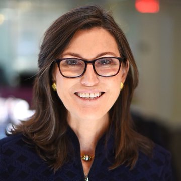 A professional headshot of a smiling woman with glasses and shoulder-length brown hair, wearing a dark patterned blazer. The image appears to be a portrait of an ARK Invest executive, accompanying news that the firm's venture fund is being tokenized on Ethereum through Securitize.