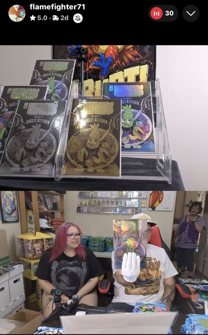A livestream screenshot from 'flamefighter71' showing a display of 'Sheel's Kitchen' collectible cards featuring food characters, with two people sitting below the display in a room filled with merchandise.