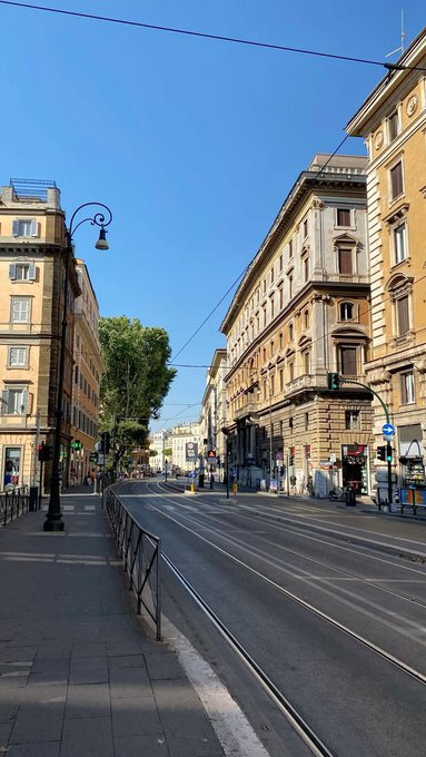 A sunny street scene in an Italian city featuring historic yellow buildings, tram tracks, and a clear blue sky.