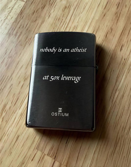 A black Zippo-style lighter on a wooden surface with engraved text reading 'nobody is an atheist at 50x leverage' and the brand 'OSTIUM' at the bottom.