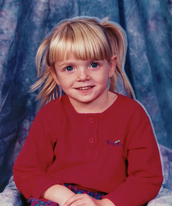 A young blonde girl with pigtails smiles for a school portrait, wearing a red shirt with "OshKosh" embroidered on it. The image playfully identifies her as the person behind the account, adding a personal touch by revealing the face behind the posts.
