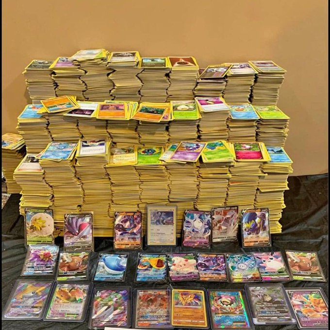Massive collection of Pokemon trading cards stacked in large piles with rare holographic cards displayed in the foreground.