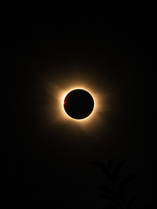A total solar eclipse is captured against a dark sky, with the sun's corona glowing brightly around the moon.