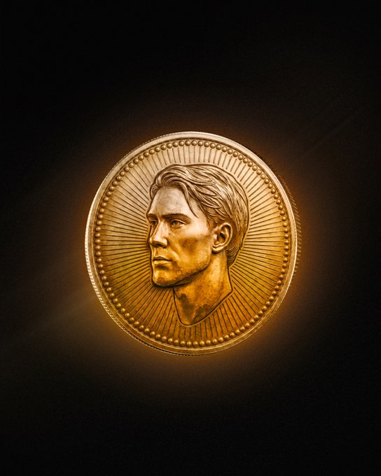 A golden commemorative coin featuring a sculpted profile portrait of a man, illuminated against a dark background.