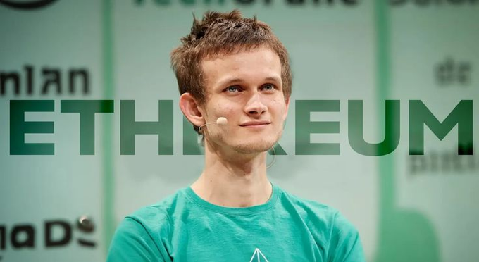 A young man with light brown hair wearing a teal Ethereum-branded t-shirt and a headset microphone stands in front of a backdrop displaying the word "ETHEREUM" in large green letters, representing Ethereum co-founder Vitalik Buterin as he discusses the intersection of AI safety and adversarial governance theory.