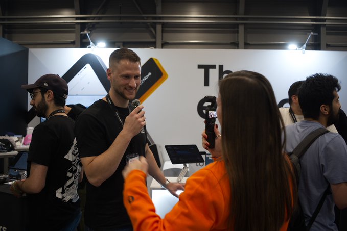 The image shows a man wearing an orange shirt standing next to a woman who has long brown hair, both holding microphones as they appear to be giving a presentation or speech at an event. The background of the image reveals that there are other people present in the room, indicating that this is likely a conference or gathering. The post about saving your financial life seems unrelated and does not have any direct connection with the scene depicted in the image.