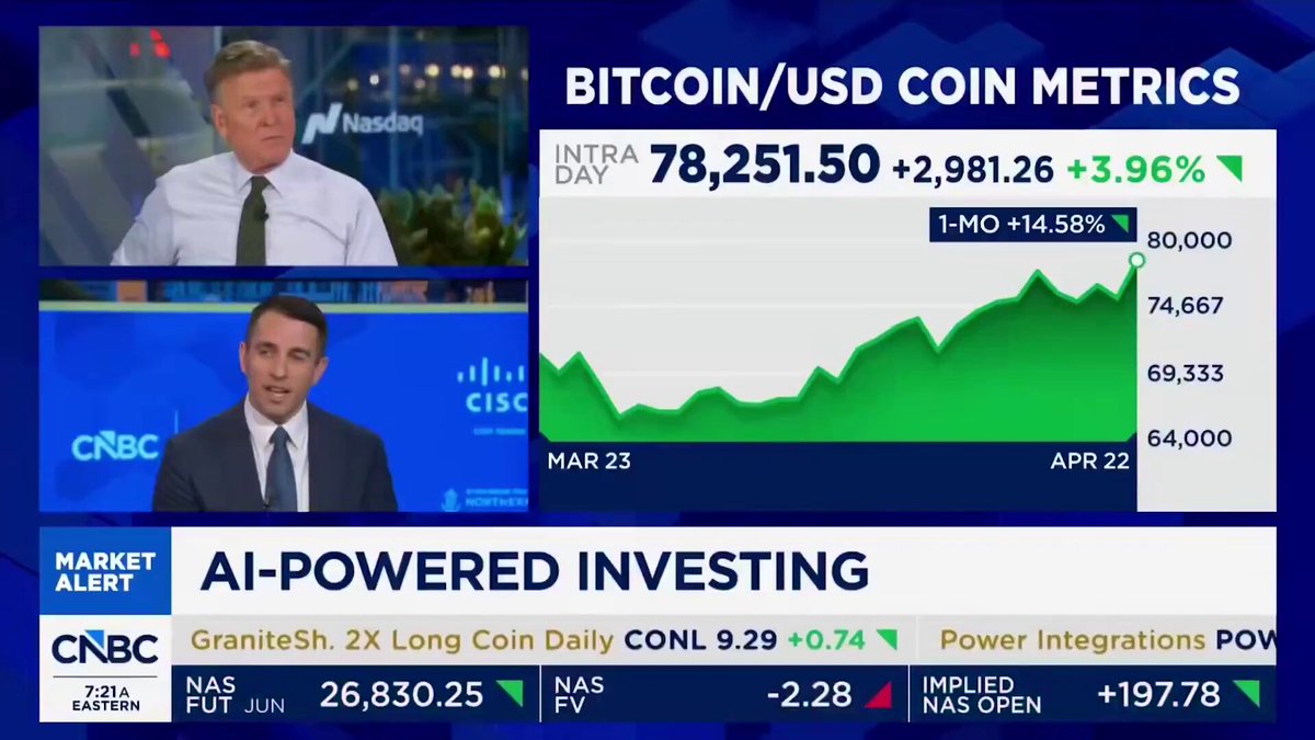 In this image, there are two men sitting on either side of a table with a television screen behind them. The focus of their conversation appears to be Bitcoin and USDC Coin Metrics. One man is wearing a tie, while the other has a more casual look. The television screen displays information about Bitcoin prices over time, as well as a bar graph showing the current value of Bitcoin relative to USDC Coin Metrics. They seem to be discussing this information or possibly analyzing it in some way.
