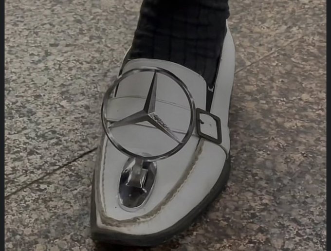 A white shoe features a Mercedes-Benz logo emblem attached to its front, with the iconic three-pointed star visible inside the circular frame, worn by someone standing on a stone-tiled floor. The image appears to be a humorous visual metaphor suggesting that the person is ready to "floor it" or accelerate once $NPC reaches a new all-time high, playing on the automotive branding.