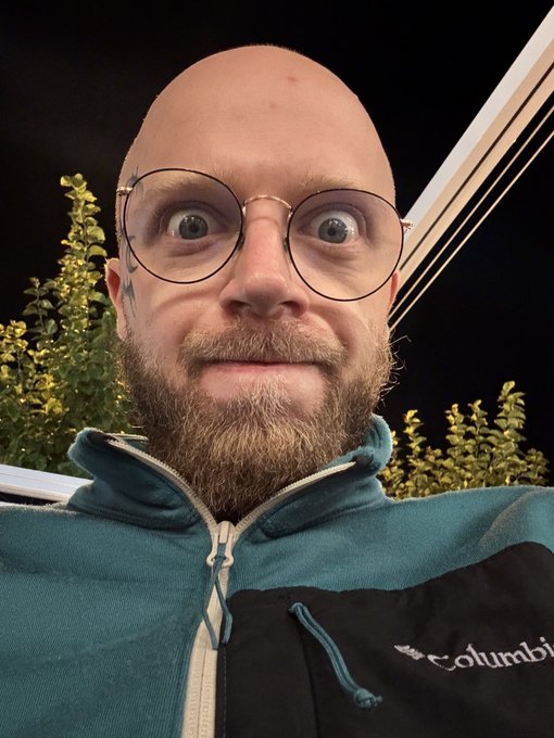 A wide-eyed, slightly frazzled-looking man wearing round glasses and a teal Columbia jacket takes a close-up selfie at night, capturing the visible effects of sleep deprivation mentioned in the post. His alert expression humorously mirrors the "rabbit hole" obsession described, as he appears wired despite running on just five hours of sleep.