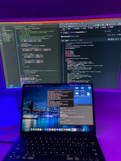 A laptop on a desk displaying coding work and a Brooklyn Bridge wallpaper, with two external monitors showing code editors and a GitHub repository for 'grod220-bot_scaffold' in the background under purple ambient lighting.