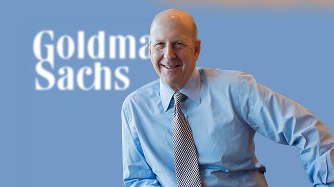 Goldman Sachs CEO David Solomon smiles in a blue dress shirt and tie, positioned in front of the Goldman Sachs logo, aligning with the firm's public push to advance the CLARITY Act for digital asset regulation.