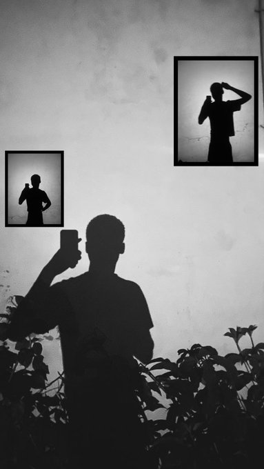 A black and white silhouette photograph of a person holding up a phone, with two framed shadow portraits visible on the wall behind them.
