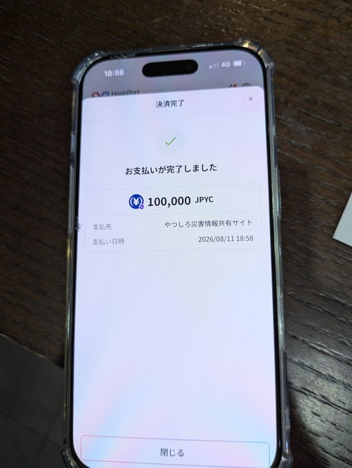 A smartphone displays a HashPort Wallet payment confirmation screen showing a completed 100,000 JPYC donation to "やしろろ災害情報共有サイト" at 18:58 on 2026/08/11, visually supporting the post's enthusiastic endorsement of donating JPYC through HashPort Wallet.