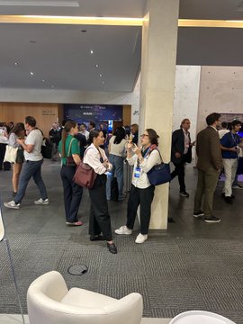 A group of people in business attire stand conversing in what appears to be a convention or conference center lobby.