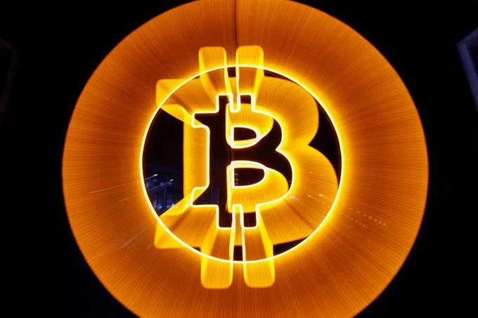 An illuminated, glowing orange Bitcoin (₿) logo sign.