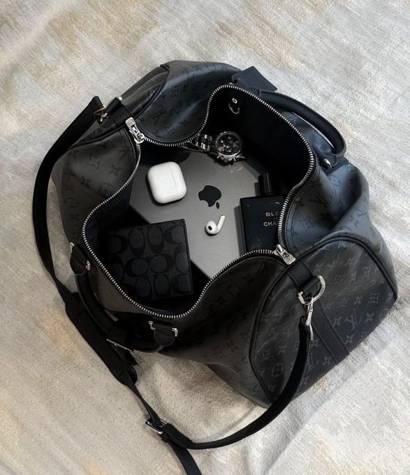 A black Louis Vuitton-patterned handbag lies open, revealing a laptop with an Apple logo, white earbuds, a wallet, and a wristwatch.