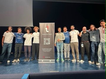 A group of about ten young people in matching white and blue t-shirts pose on stage behind an 'Avalanche Squad' banner featuring a QR code.