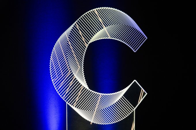 A large, illuminated wireframe sculpture of the letter "C" is displayed against a dark background lit with blue ambient lighting. The stylized letter likely represents "Canton," visually reinforcing the post's theme of a unified ecosystem gathering at the Canton Summit.