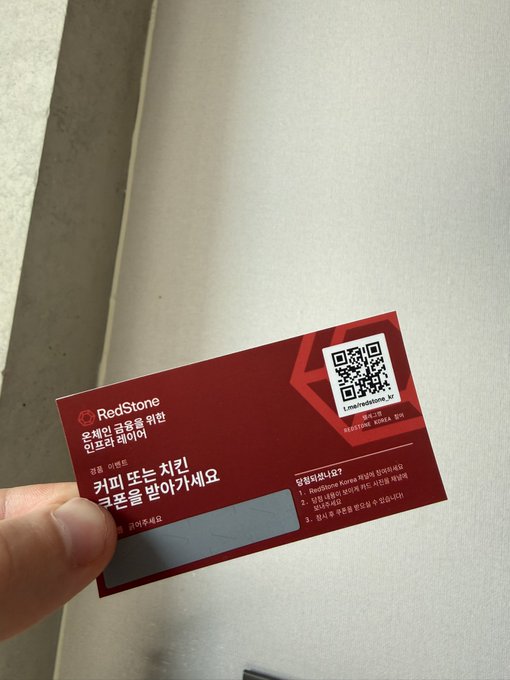 A hand holding a RedStone (i.m.redstone.kr) Korean loyalty member card with a QR code, featuring Korean text thanking customers for banking with them and providing a lottery ticket.