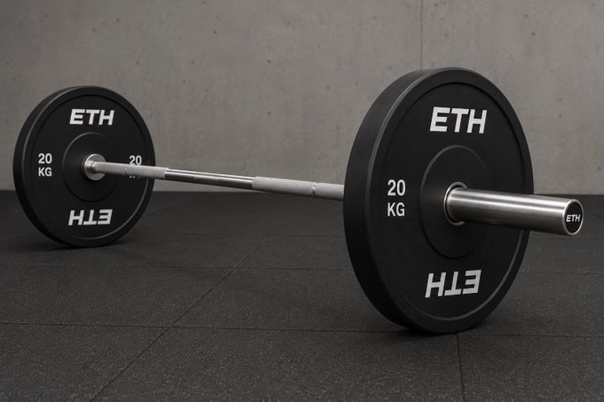 A black barbell weight plate labeled "ETH" with "20 KG" weight markings sitting on a gym floor against a concrete wall.