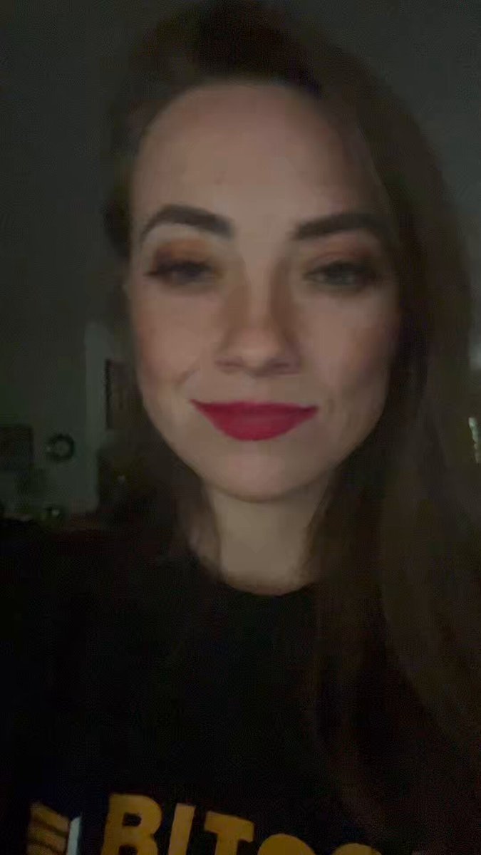The image features a woman wearing a black shirt that says "BITCOIN" on it. She has long brown hair, and she's smiling at the camera while looking directly into it. Below her photo, there is text that reads "@kit_sats reached out to me after realizing we had a mutual connection... the scammer." This message seems to be a warning or cautionary tale about potential online scams involving people with similar interests in cryptocurrency.