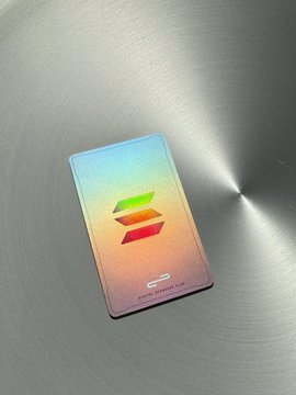 A metallic Solana (SOL) branded card with an iridescent rainbow finish resting on a brushed steel surface.
