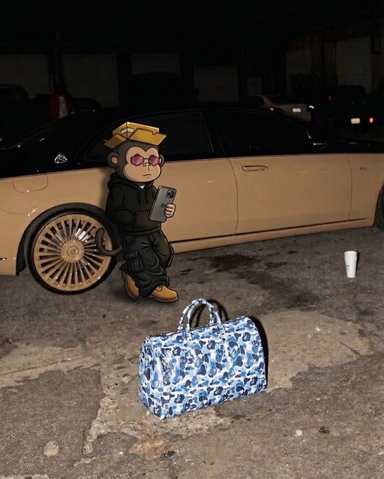 A cartoon monkey character wearing sunglasses, a gold hat, and black clothing stands next to a tan car while holding a smartphone, with a blue camouflage duffel bag on the ground nearby.