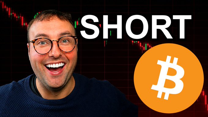 A man with glasses and a beard smiles enthusiastically on the left side of a thumbnail, with the large text "SHORT" above him and an orange Bitcoin logo on the right, set against a dark background with red and green candlestick chart patterns.