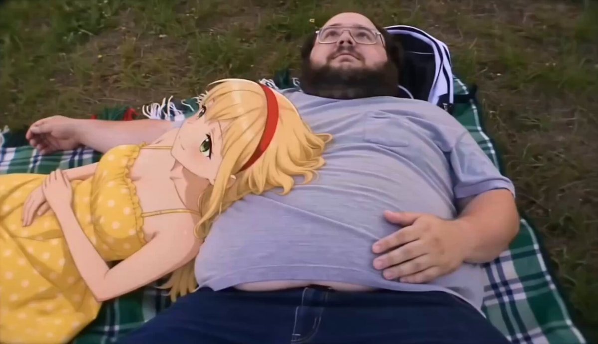 The image features a man laying down on a blanket, with a woman sitting next to him. The man has a large belly and appears to be wearing glasses. They are both lying on their stomachs, enjoying each other's company. In the background of the image, there is text that reads "Go check out the PumpFun stream if you haven't. pump.fun/coin/82MmG1uH2 ...". This suggests that they might be watching a movie or show related to pumping fun and possibly discussing it while relaxing on their blanket in the park.