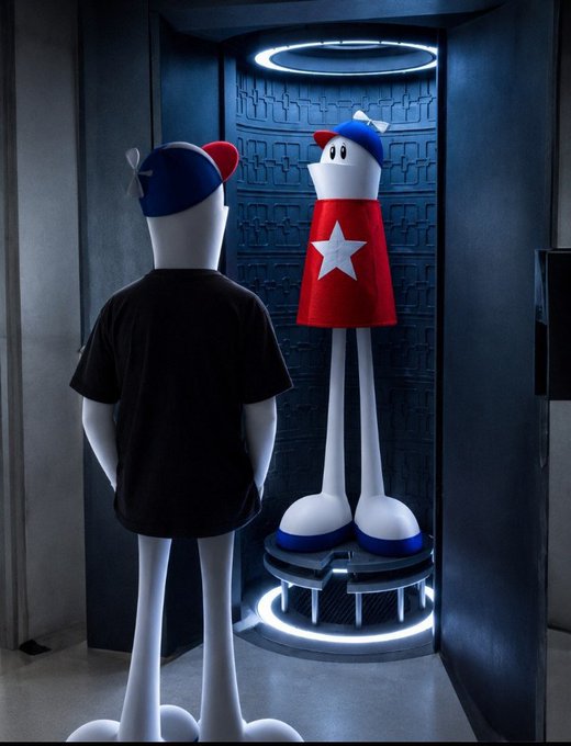 A 3D rendered scene showing two cartoonish character figures—one wearing a black shirt with a blue cap seen from behind, and another in a red outfit with a white star—standing in what looks like a sci-fi chamber or elevator.